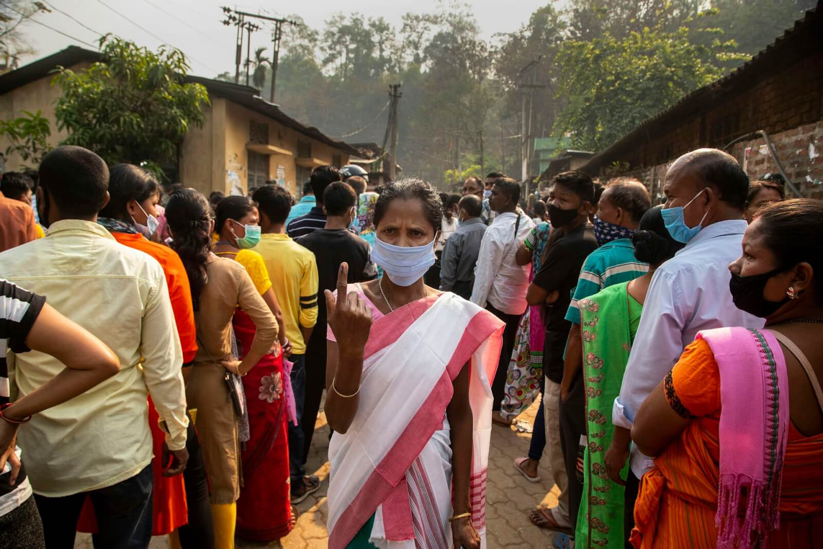 A Dalit woman stands in the middle of a crown with her pointer finger up, showing the black mark on her nail of someone who has just voted.